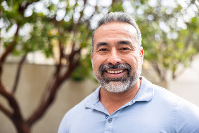 Man with a beard and mustache wearing a light blue shirt outdoors.