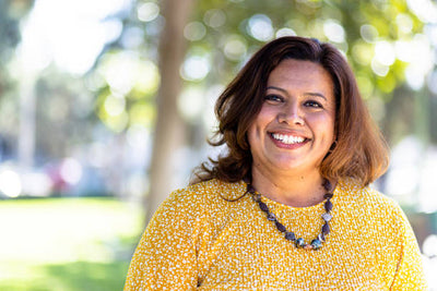 Woman in a yellow top smiling outdoors with greenery in the background